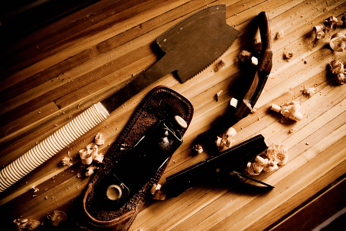 Detailaufnahme von traditionellem Handwerkzeug auf einer Holzplatte mit Holzspänen, in warmem Licht.